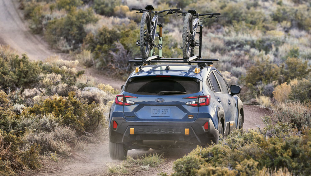 Rear shot of 2024 Crosstrek Wilderness driving with bicycles on roof racks along dusty trail.