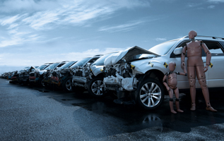 Crashed vehicles lined up with two crash test dummies standing beside a damaged car.