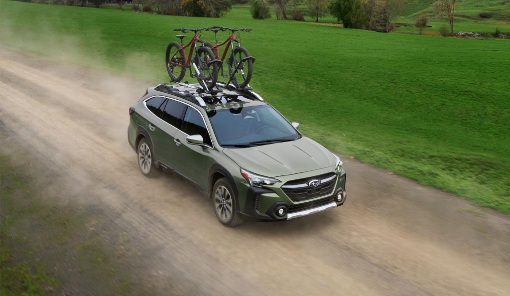 2024 Outback Premier XT on gravel road with two bicycles on roof.