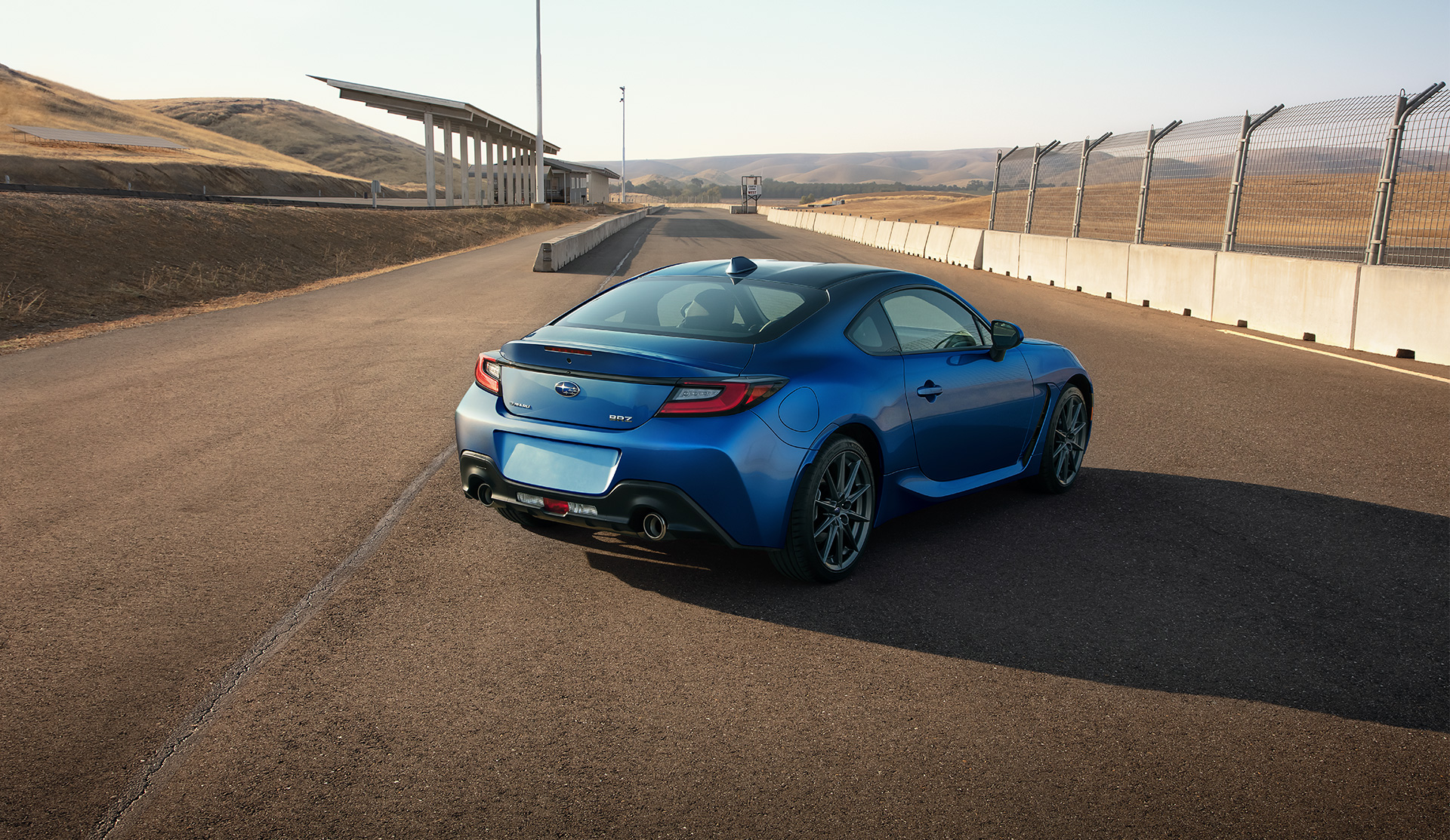 Rear view of the 2024 BRZ parked by the fence at the race track.