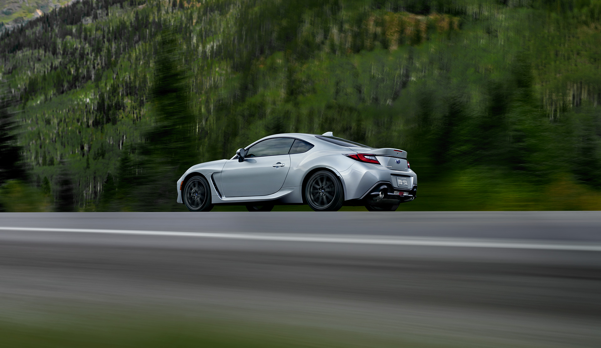 Rear quarter shot of 2024 BRZ driving on a country highway.