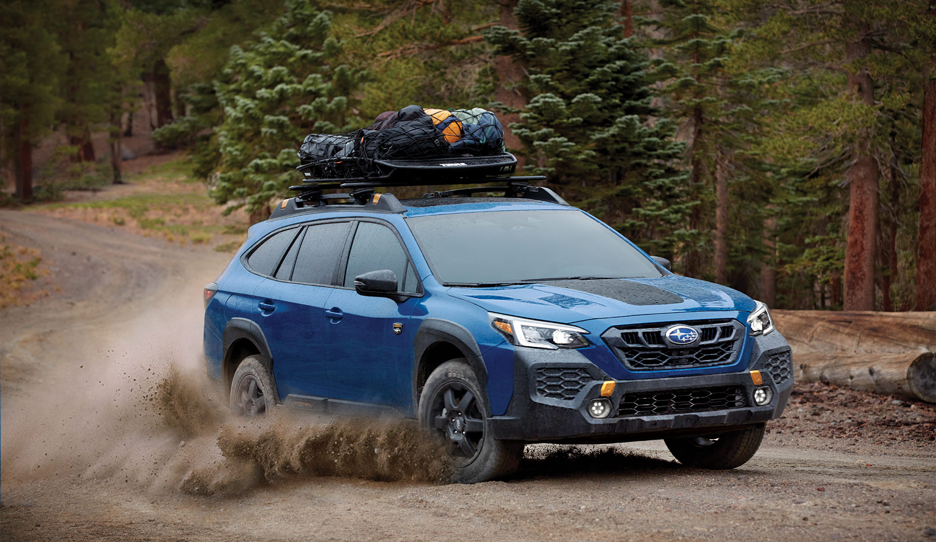 2024 Outback Wilderness driving on gravel road with cargo basket on the roof.