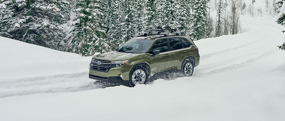 2026 Subaru Forester Hybrid Premier driving along a curved road in a snowy winter landscape.