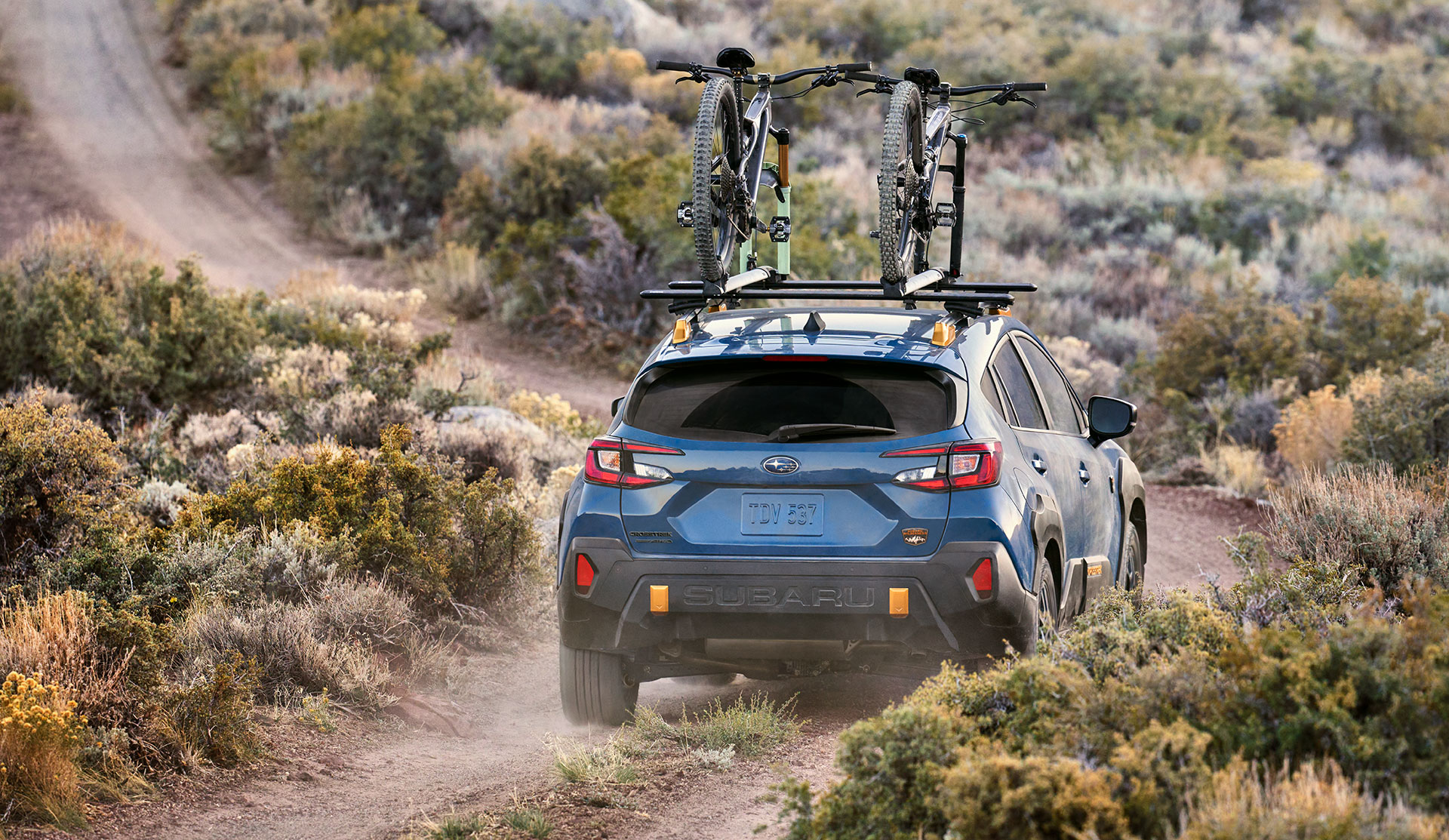 Vue arrière de la Crosstrek Wilderness 2024 transportant des vélos sur le toit, sur une route poussiéreuse.