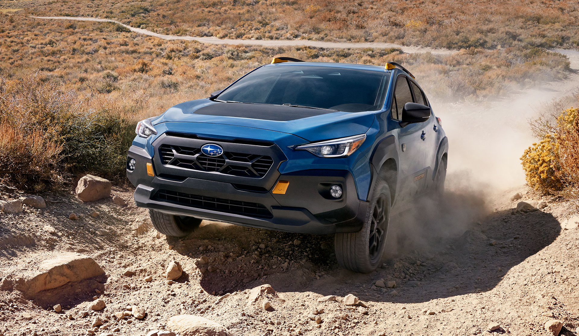 Front shot of 2025 Crosstrek Wilderness driving up dusty trail.