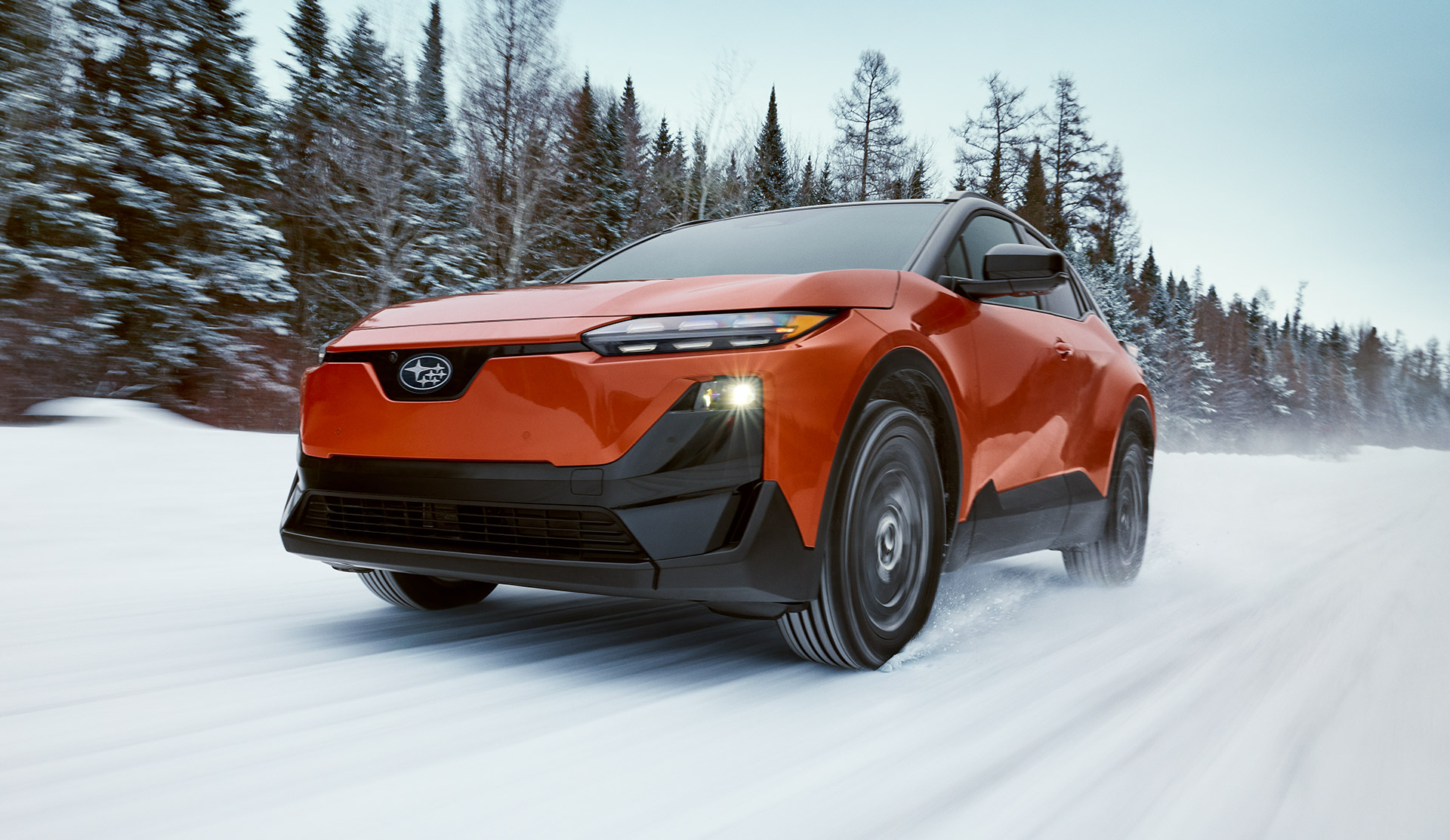 2026 Subaru Uncharted drives through a snowy forested road, kicking up snow as it moves forward under a cloudy sky.