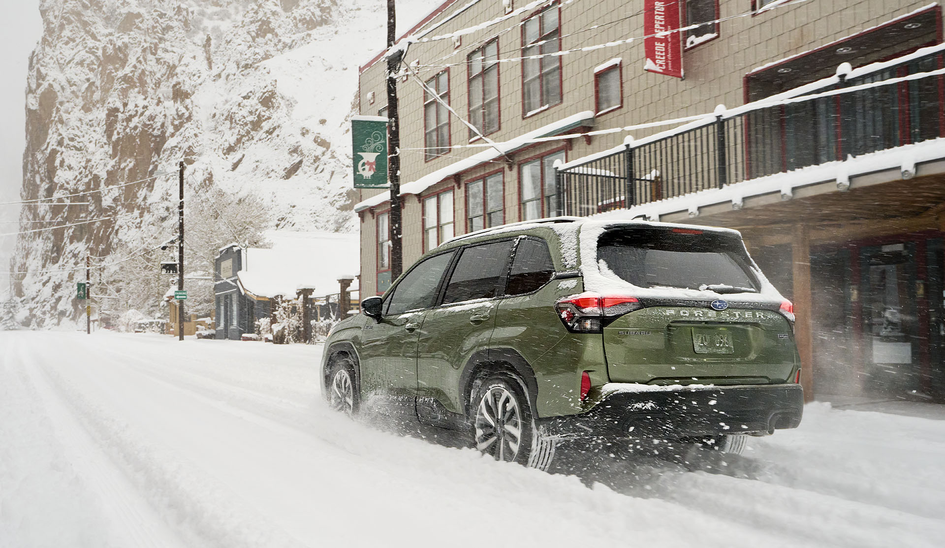 Rear view of the 2025 Forester e-BOXER Hybrid driving through snowy town street.