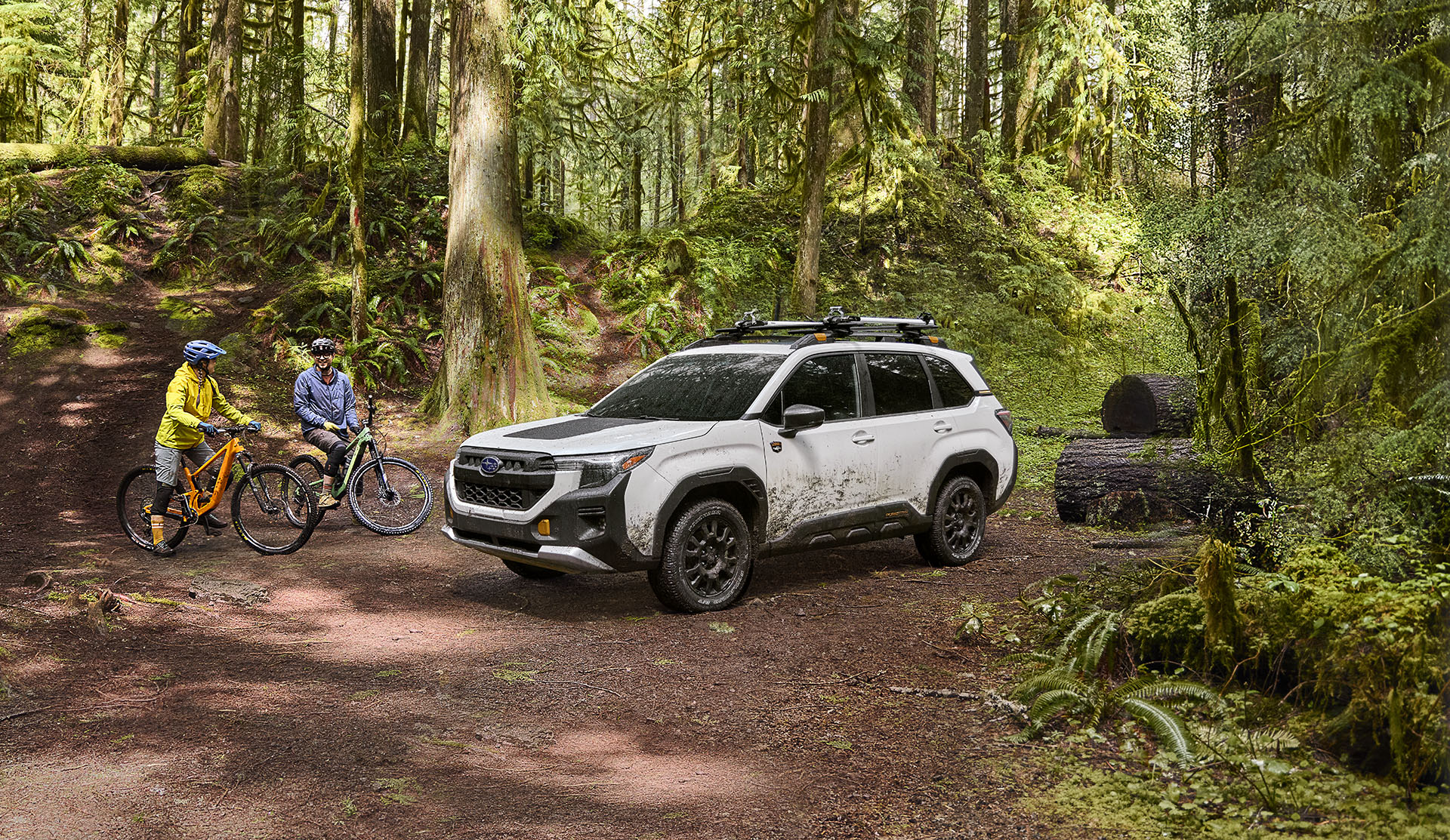 Parked 2026 Subaru Forester Wilderness in a wooded area with 2 cyclists next to it. 